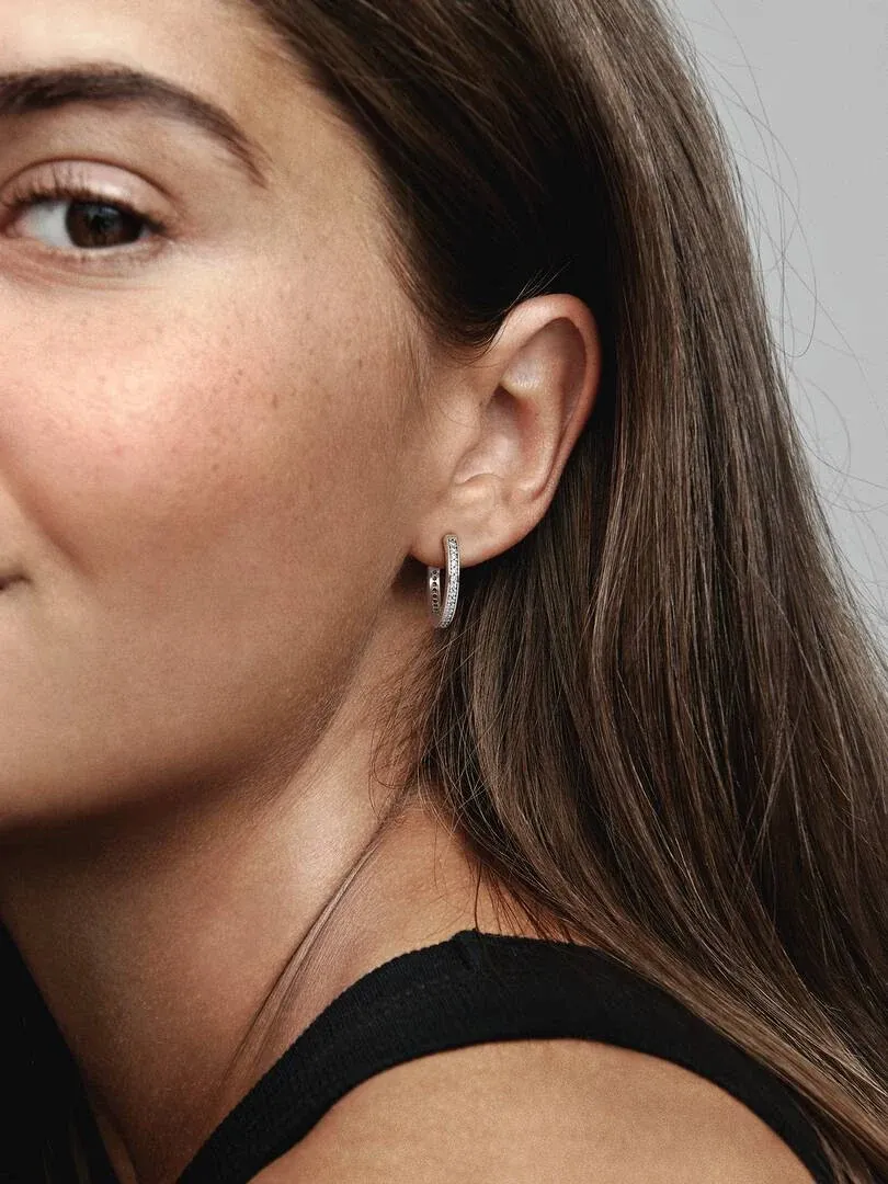 Gros plan de profil de boucles d'oreilles créoles avec logo, portées sur l'oreille d'un modèle.