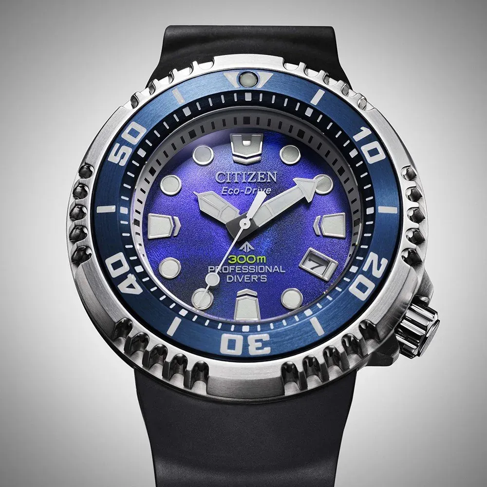 Vista frontal completa del reloj con esfera azul y correa negra sobre fondo gris neutro
