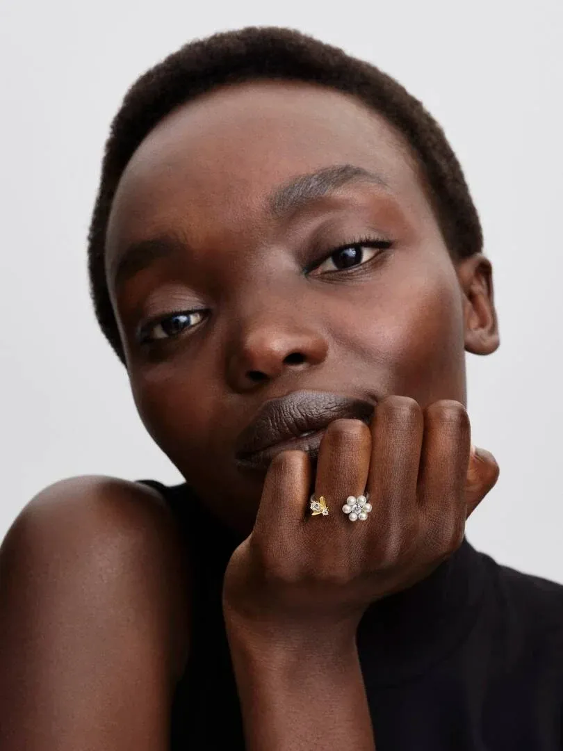 Primer plano de anillo abierto con abeja y flor sobre el dedo, modelo apoyando la barbilla en su mano.