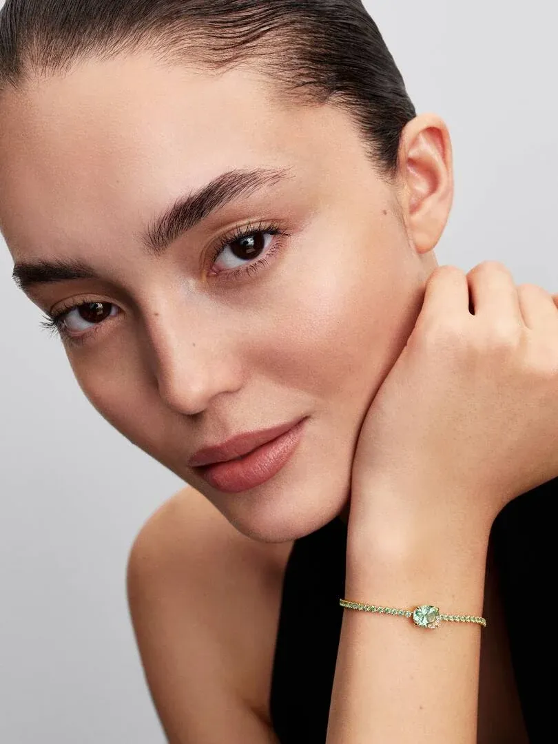 Primer plano de pulsera con cristales verdes en la muñeca, toma lateral con modelo sobre fondo gris claro.