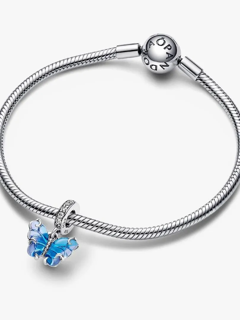 Charm papillon bleu suspendu à un bracelet en argent, vue de profil sur fond blanc.