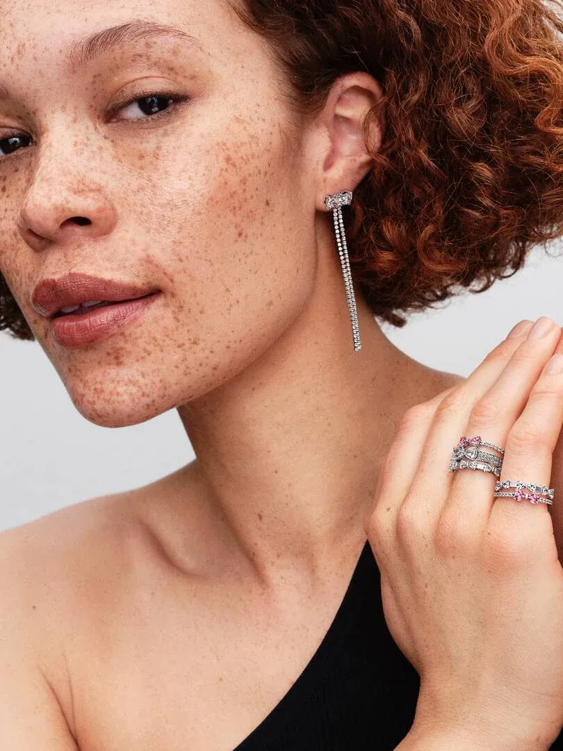 Close-up of model wearing drop earrings and two silver rings with pink stones on her hand.