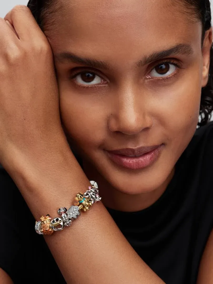 Primer plano de una muñeca con pulsera de charms, toma lateral sobre fondo oscuro y desenfocado.