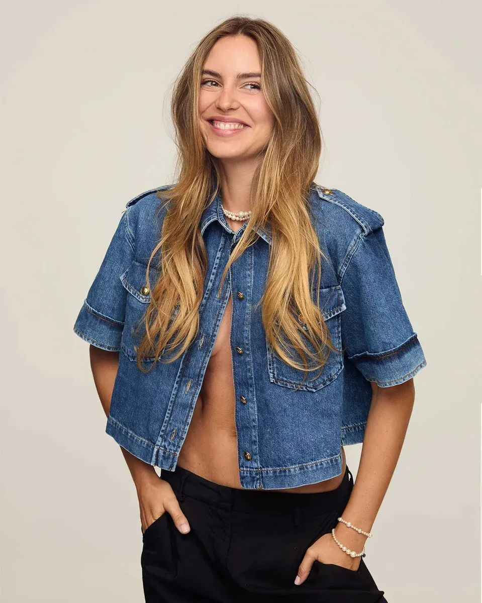 Model in open denim overhemd met parelketting en bijpassende armband, neutrale achtergrond.