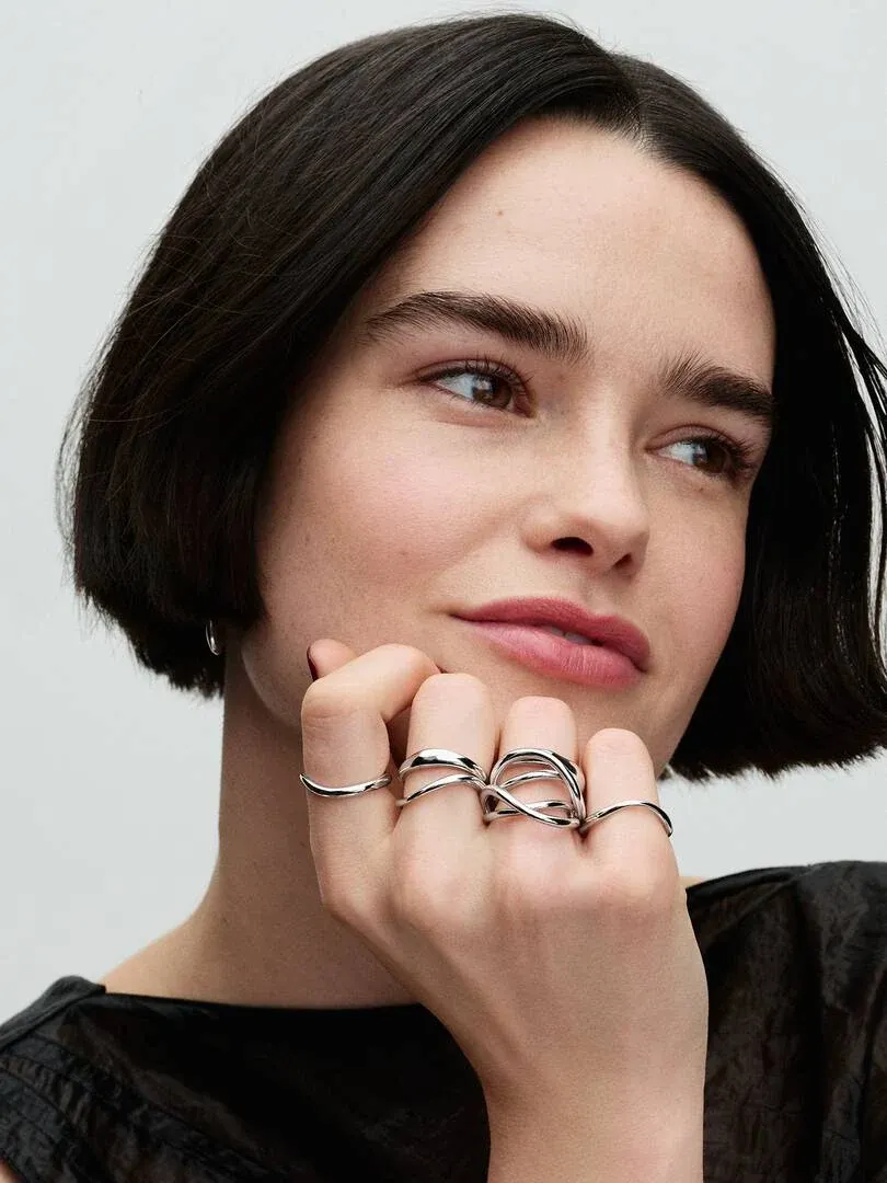 Primer plano de anillos de plata con formas orgánicas puestos en los dedos, mano apoyada en la barbilla.