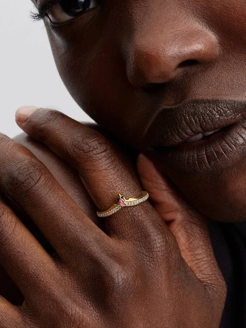 Primer plano del anillo tipo tiara con gema rosa en el dedo, toma lateral sobre piel de modelo.