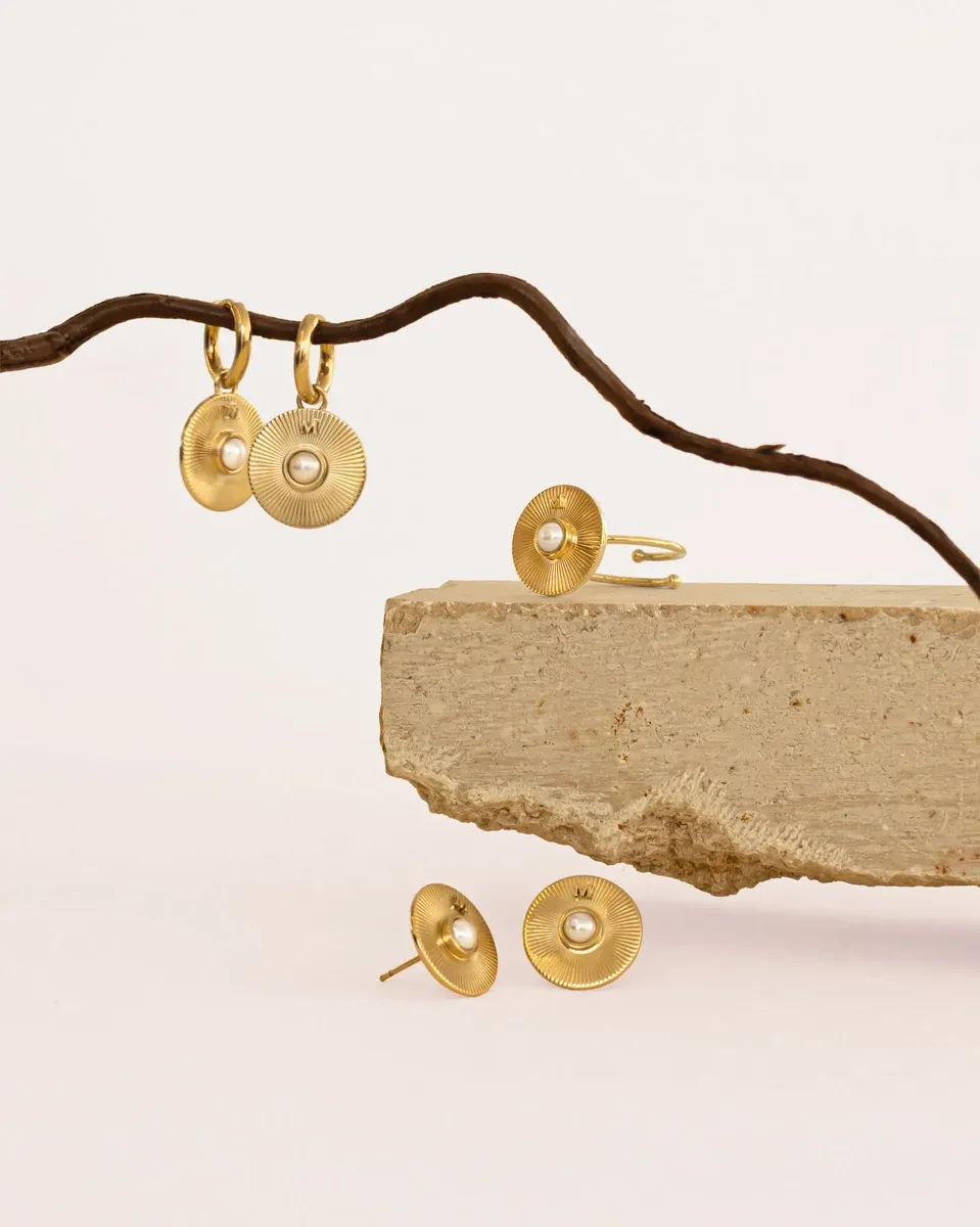 Conjunto de pendientes y anillo sobre rama y piedra natural, fondo blanco, composición artística.