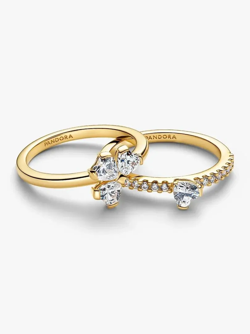 Vista frontal de dos anillos entrelazados con gemas en forma de corazón, fondo blanco.