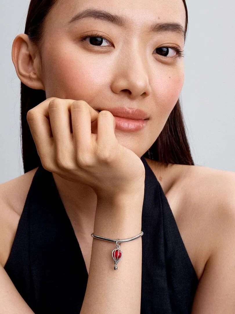 Close-up van de pols met de rode ballon charm, model in zwarte top tegen een neutrale achtergrond.