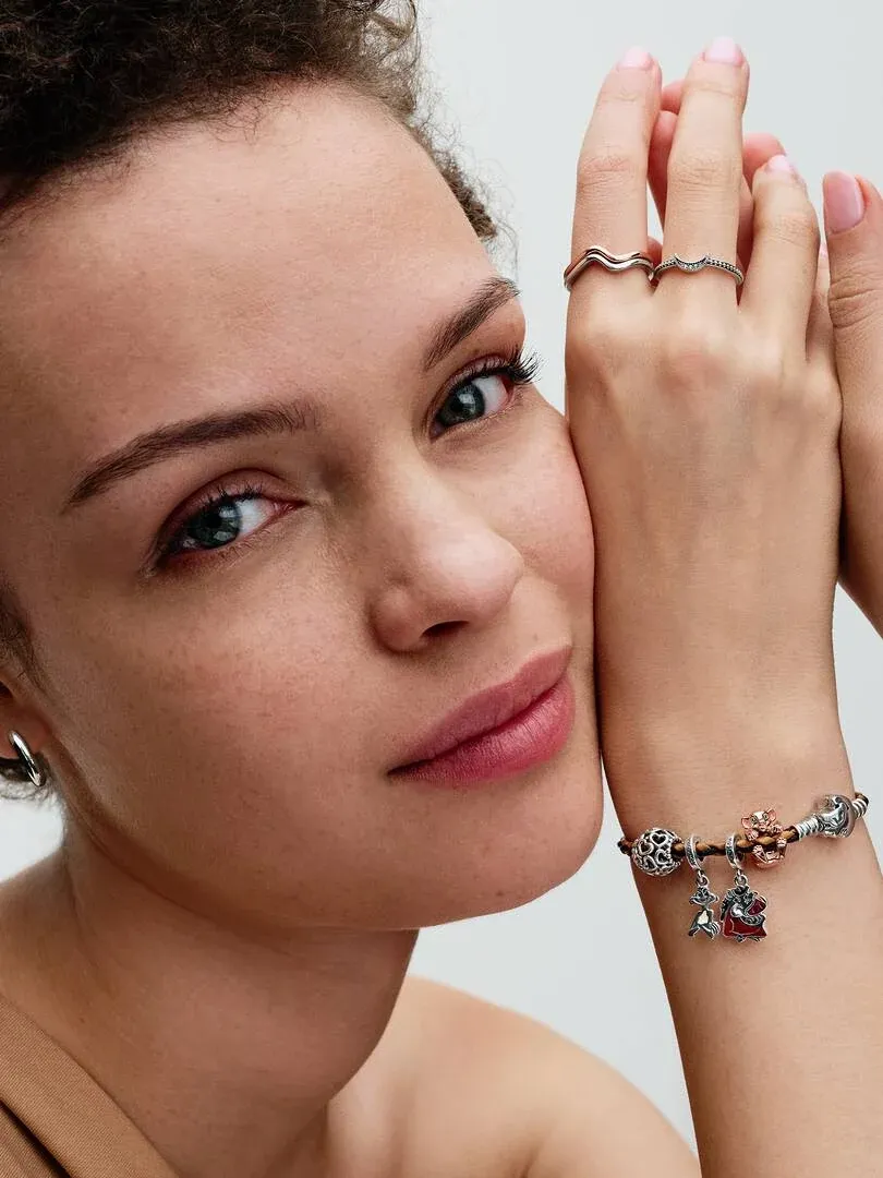 Gros plan du poignet portant un bracelet en cuir avec charms, près du visage d'un modèle sur fond neutre.