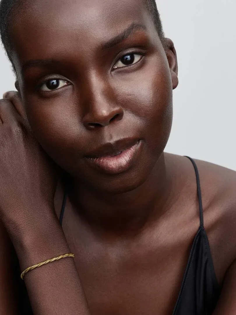 Primer plano de la pulsera dorada en la muñeca, toma lateral con modelo sobre fondo neutro claro.