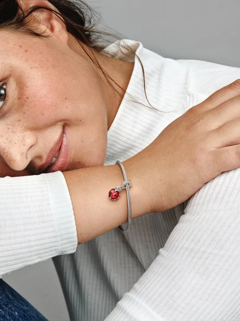 Close-up van pols met armband en rode lieveheersbeestjes charm, op witte mouw, zijaanzicht.