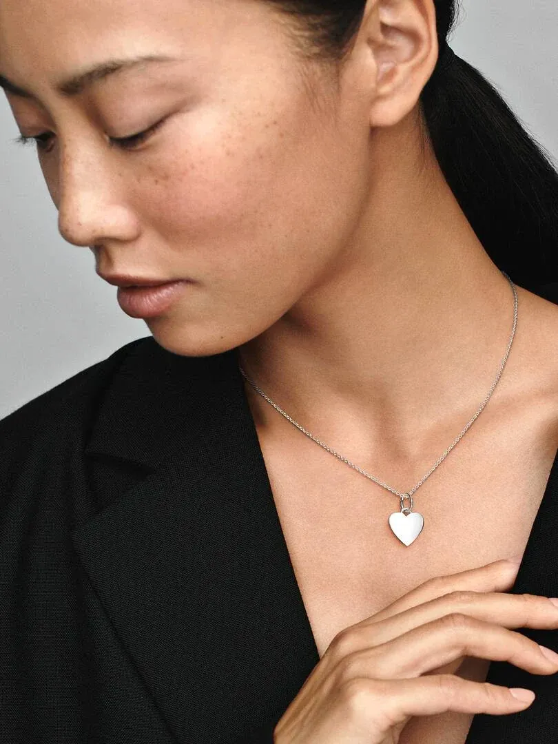 Primer plano de colgante de corazón de plata sobre el cuello de una modelo, toma lateral con fondo neutro.