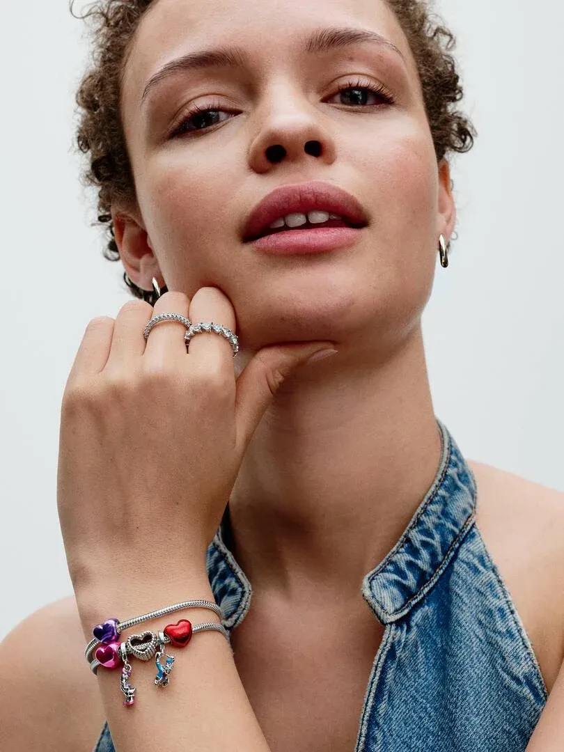 Gros plan d'un modèle portant des créoles, des bagues et un bracelet à charms, fond blanc neutre.