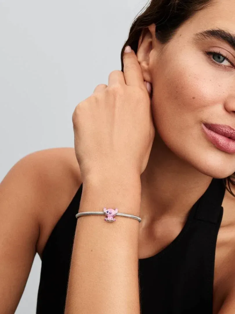 Primer plano de la muñeca con el charm de Angel rosa en una pulsera de plata, sobre fondo neutro.