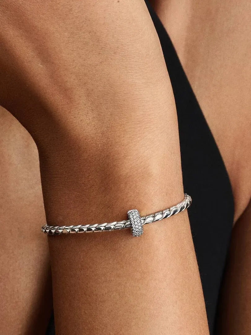 Close-up van de armband met pavé clip charm om een pols, zijaanzicht tegen een donkere achtergrond.