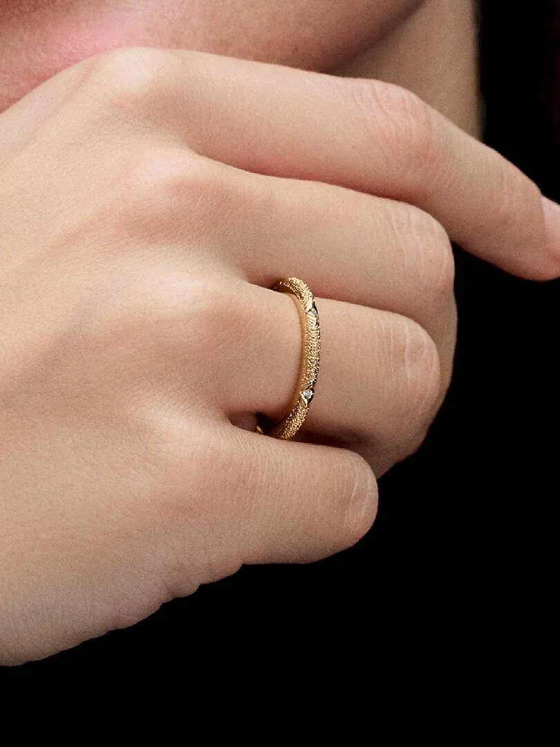 Primer plano lateral del anillo dorado con circonitas puesto en el dedo, fondo negro sólido.