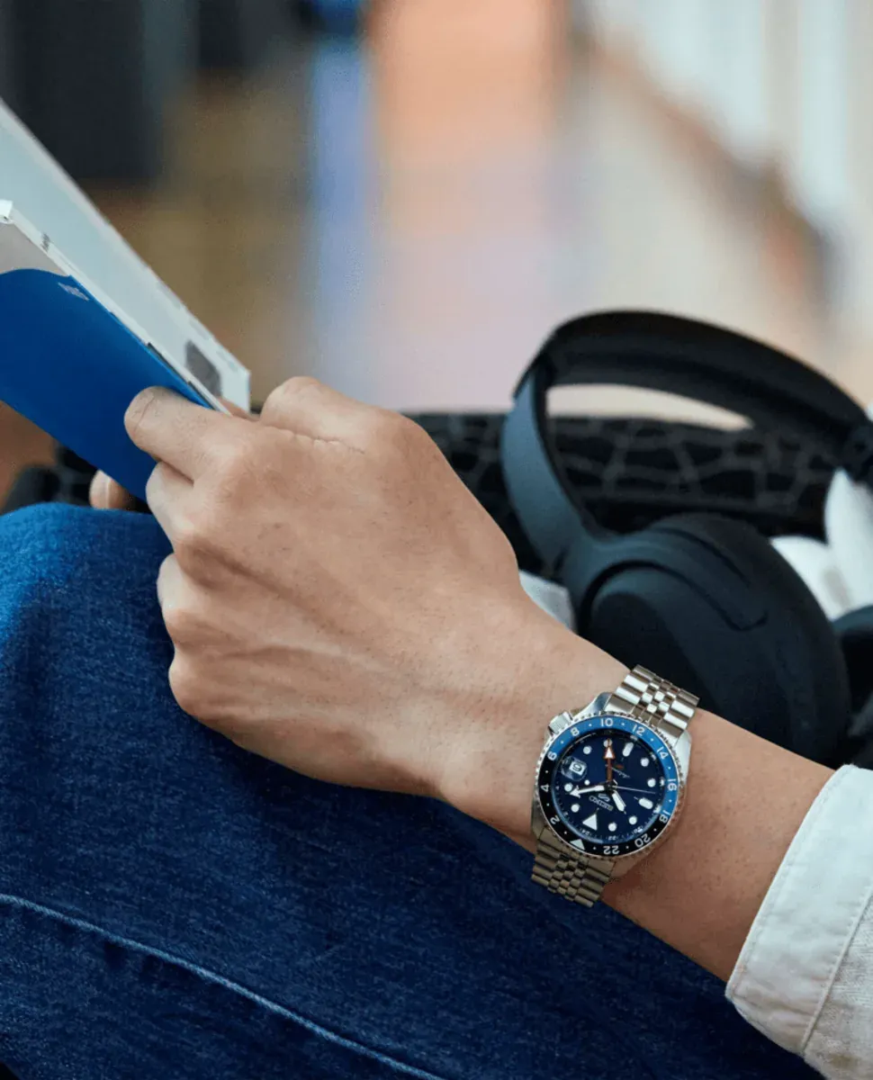 Reloj puesto en muñeca masculina, toma lateral en contexto cotidiano con tablet y auriculares, fondo desenfocado