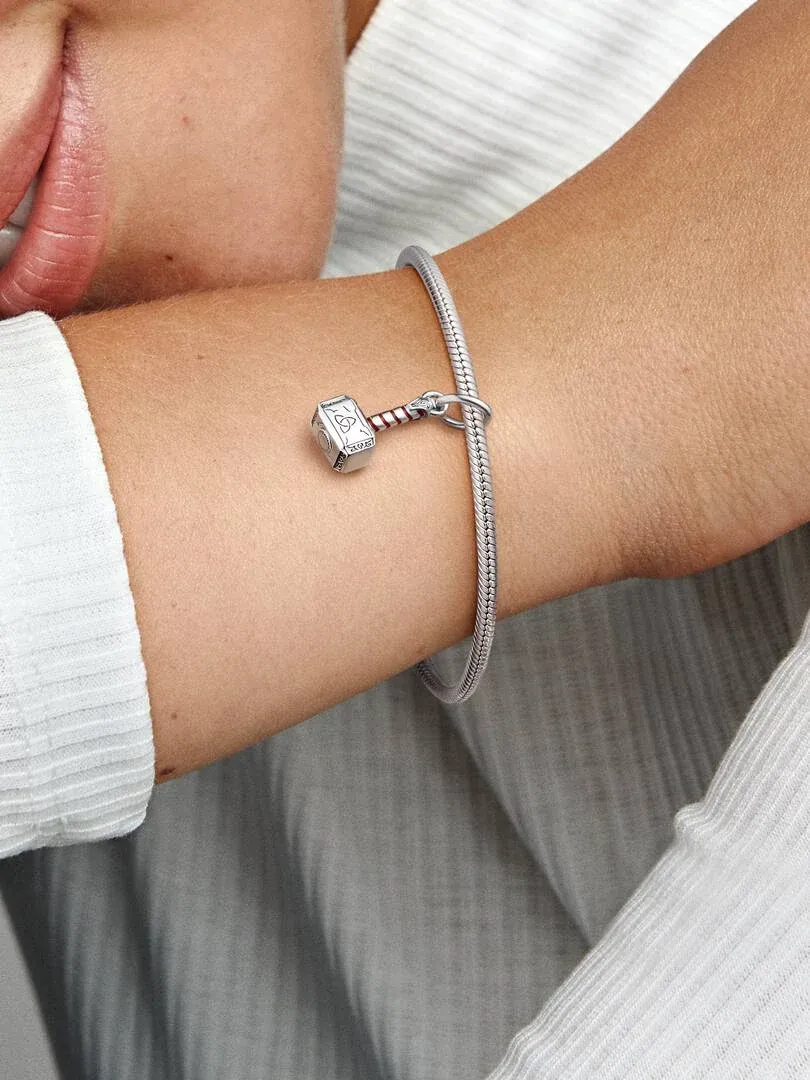 Primer plano del charm de martillo en una pulsera de plata, puesto en la muñeca con fondo neutro.