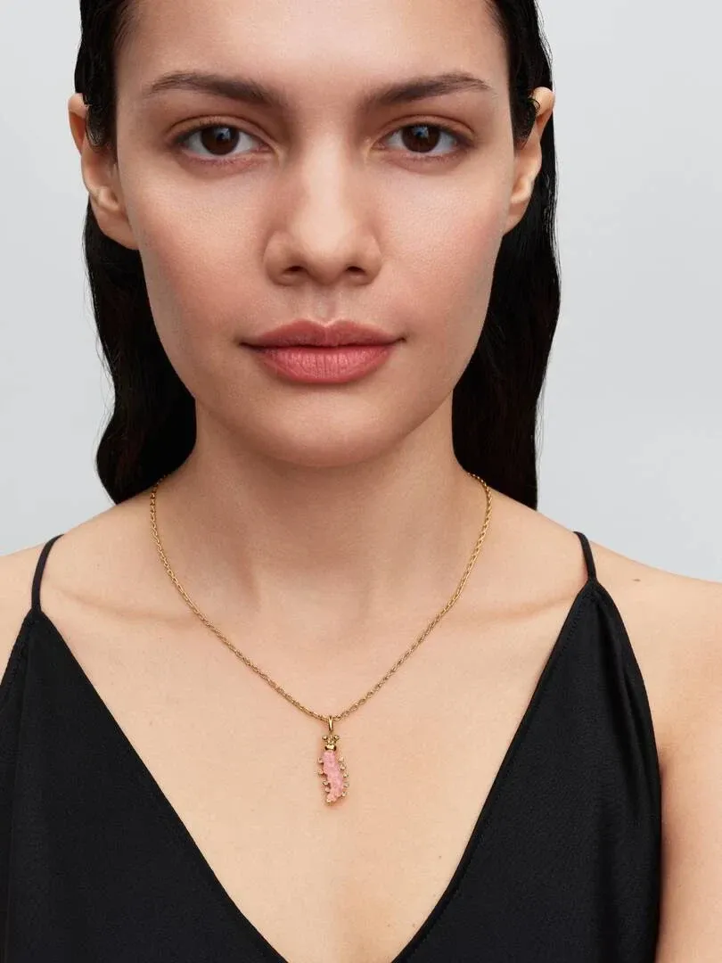 Close-up van een ketting met roze rups hanger om de hals van een model, neutrale achtergrond.