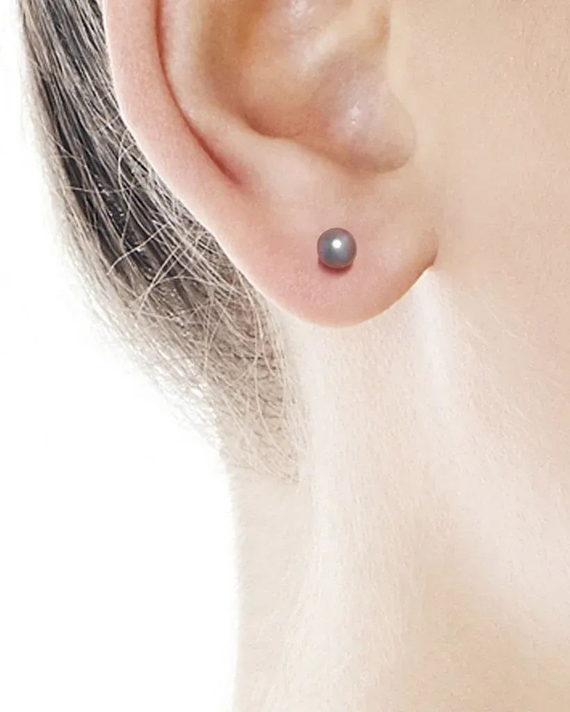 Close-up of a grey pearl stud worn on the earlobe, side view against a light background.