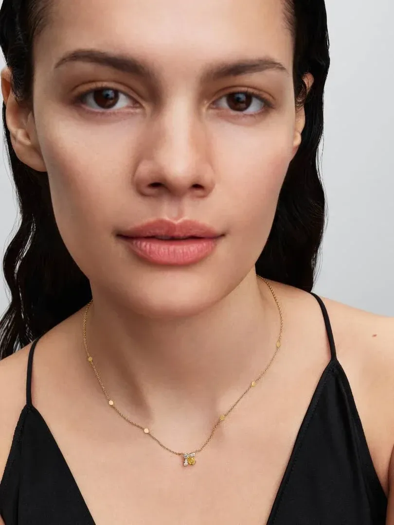 Gros plan du collier avec pendentif abeille jaune porté sur le cou d'un mannequin, fond neutre.