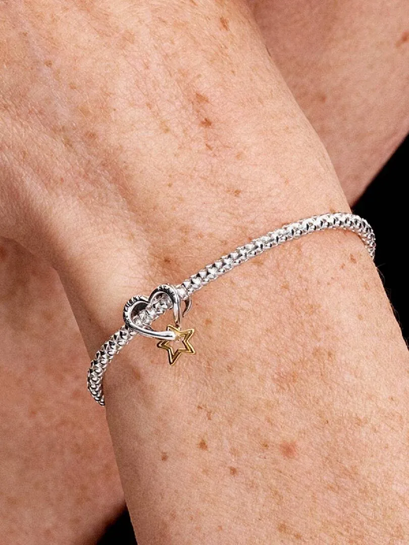 Gros plan du charm étoile et cœur sur un bracelet, porté au poignet.