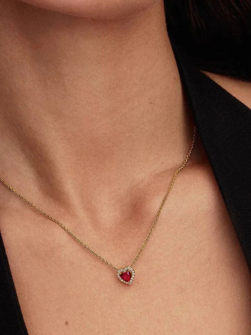 Gros plan du collier avec pendentif cœur rouge sur le cou d'un mannequin, fond sombre.