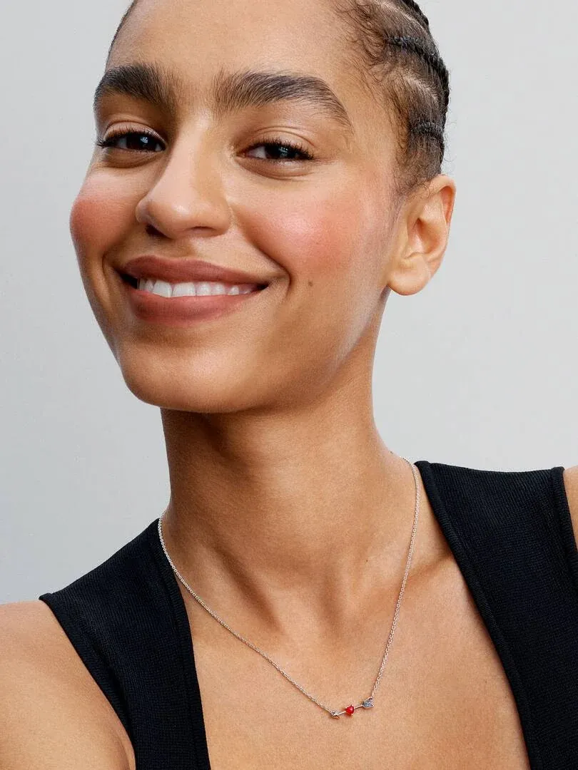 Close-up of the necklace with red pendant on a model's neck, light neutral background.