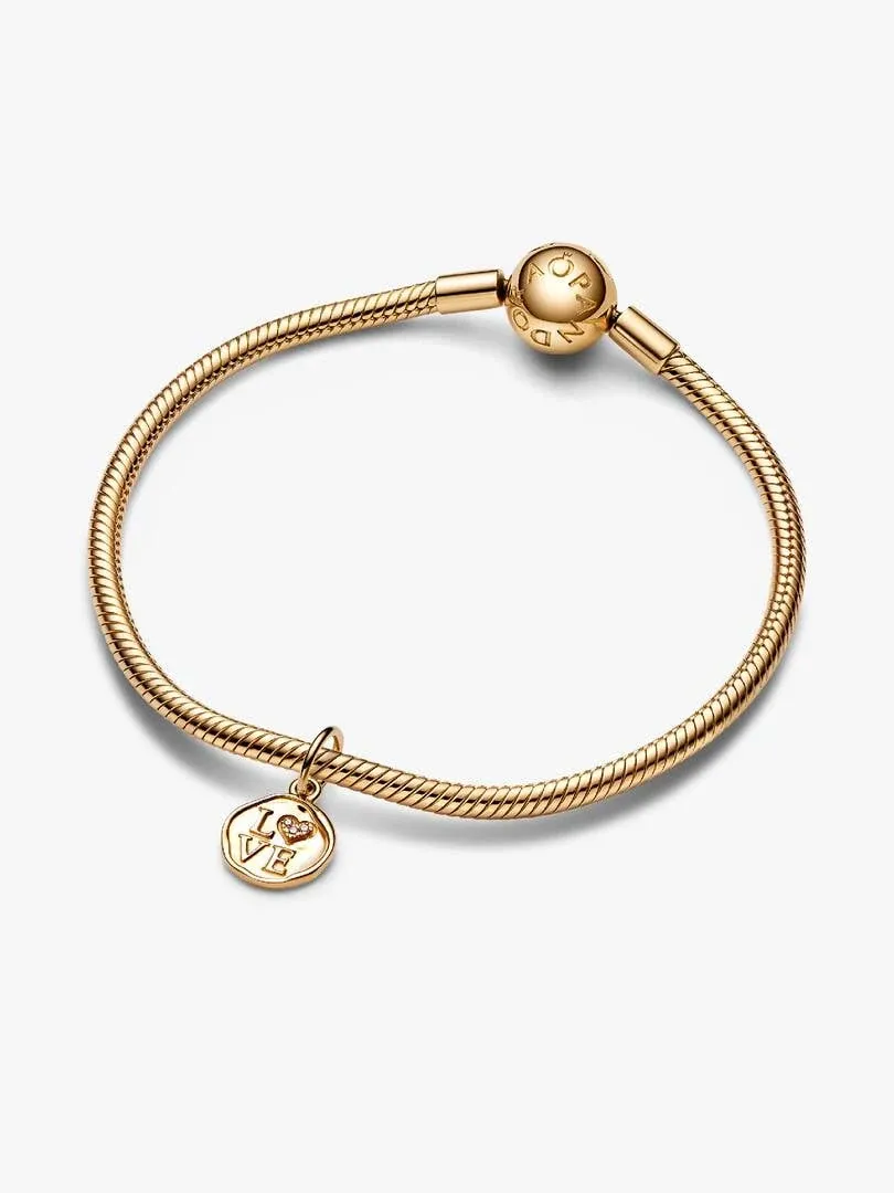 Pulsera de oro con charm colgante visto desde un ángulo superior sobre fondo blanco.