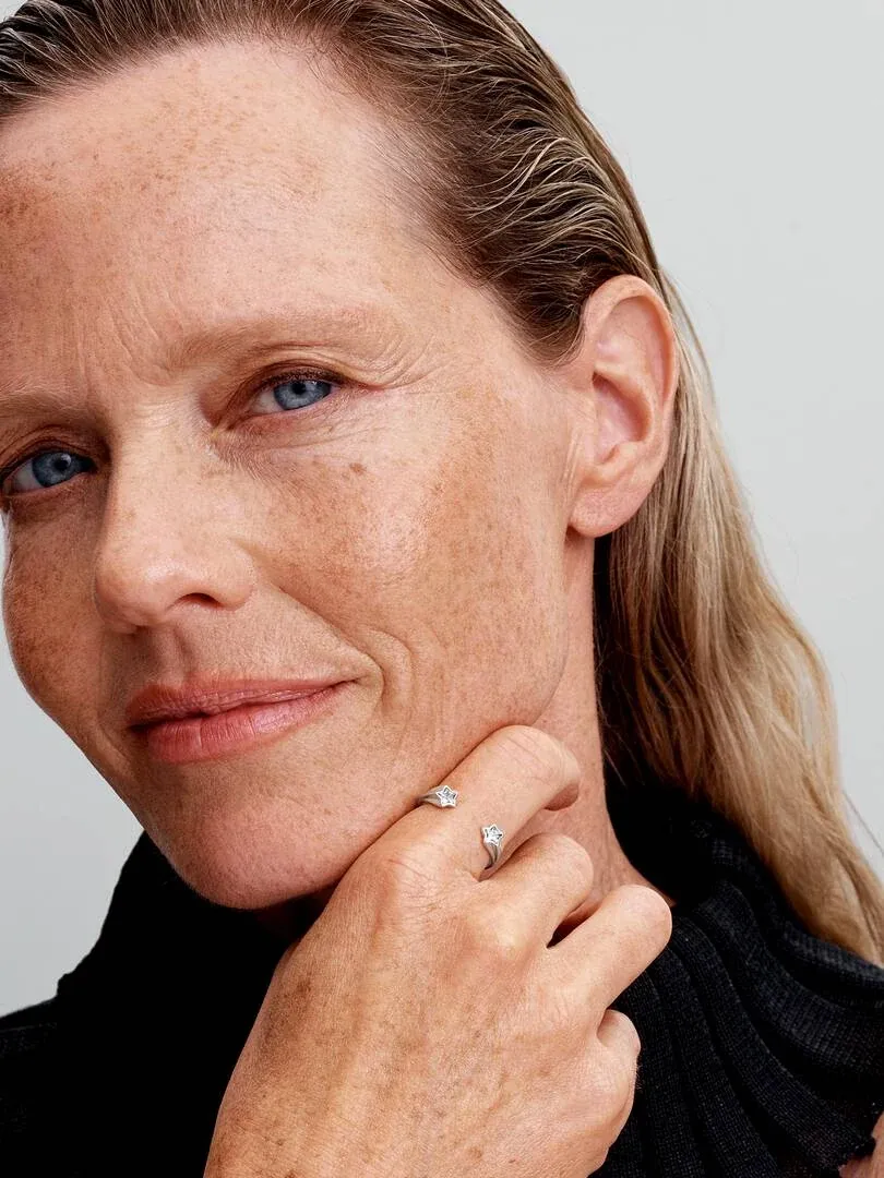 Close-up of a female hand wearing an open silver ring, side view resting against the cheek.