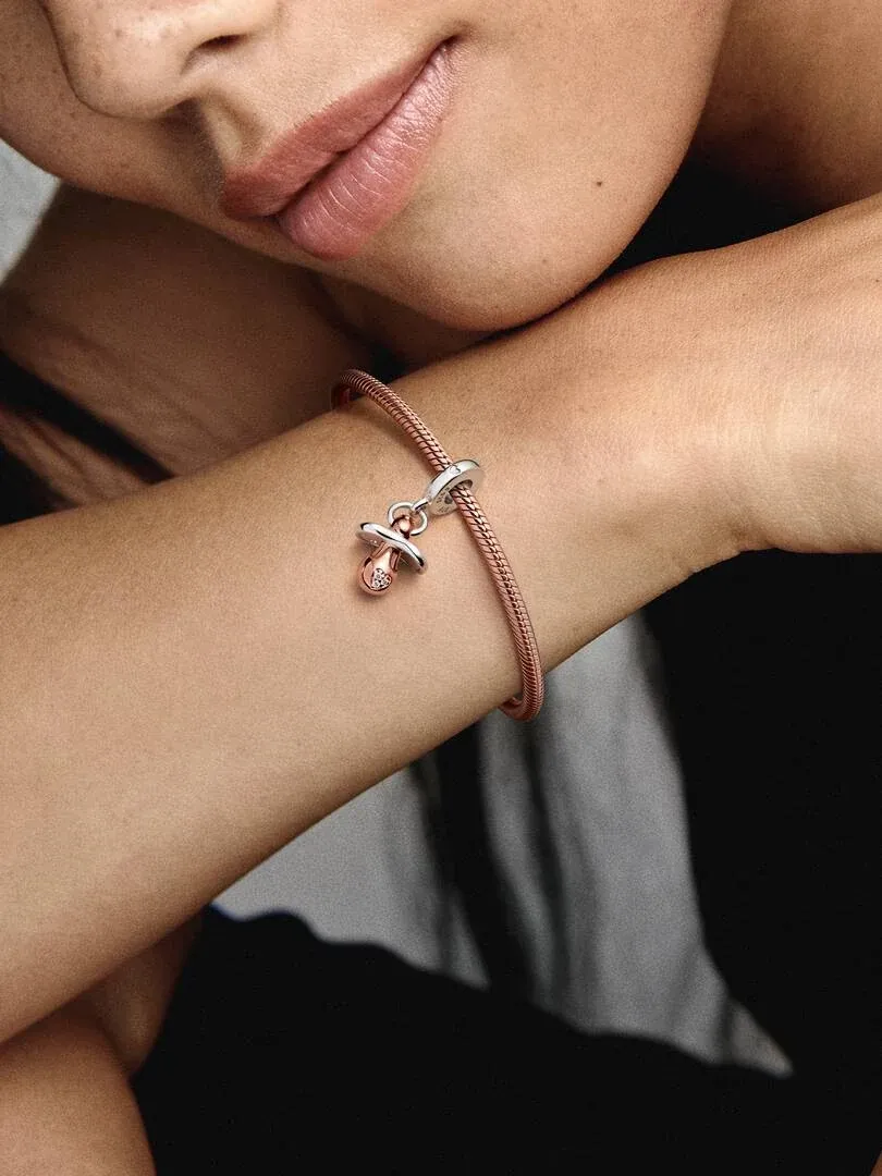 Primer plano del colgante de chupete en oro rosa sobre una pulsera, luz natural en la muñeca de una modelo.