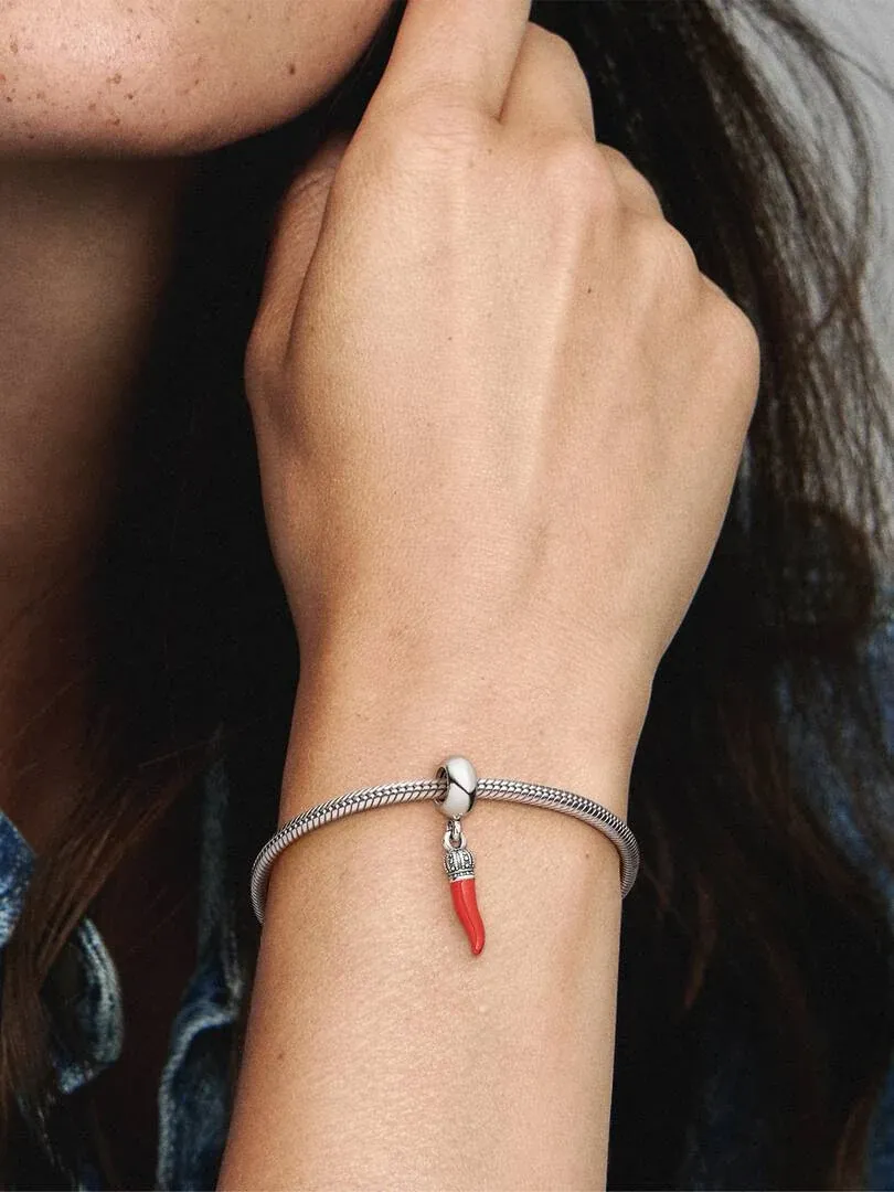 Gros plan d'un charm pendant rouge sur un bracelet en argent, porté au poignet d'un modèle.