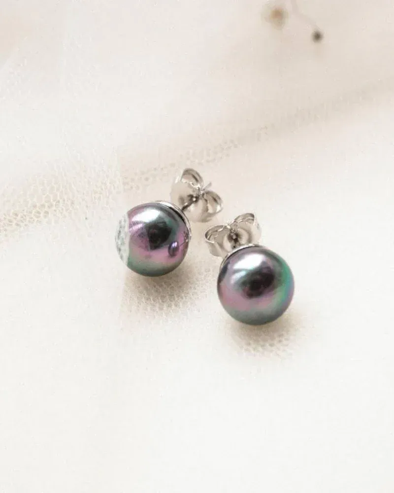 Pendientes de perla gris dispuestos sobre tela blanca texturizada, toma cenital con luz suave.