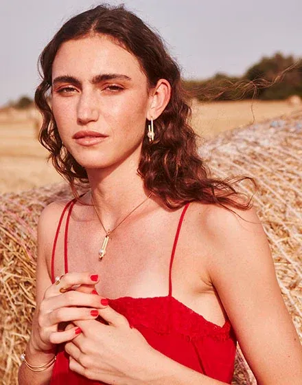 Close-up van model met gouden oorbellen en ketting, wazige achtergrond van een stroveld.