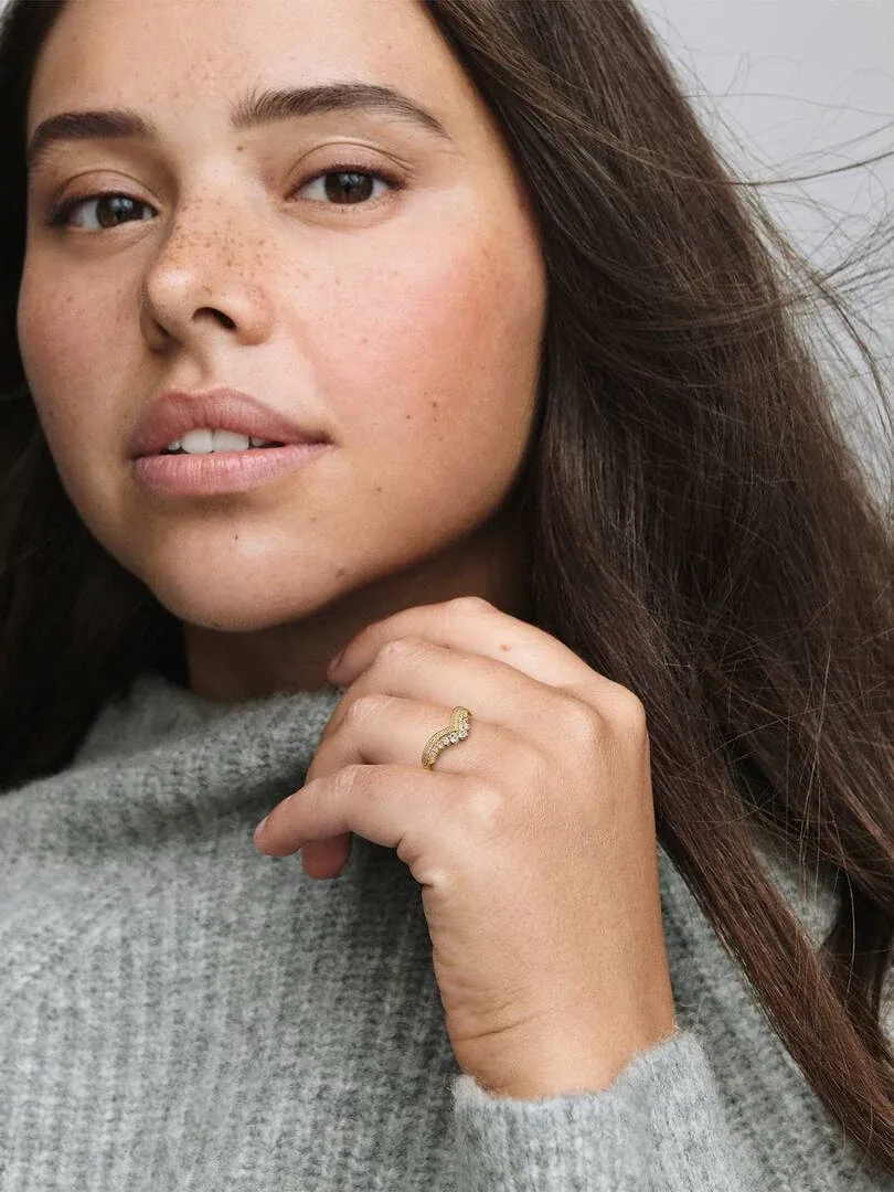 Primer plano del anillo de tiara en el dedo anular, modelo con jersey gris y fondo neutro.