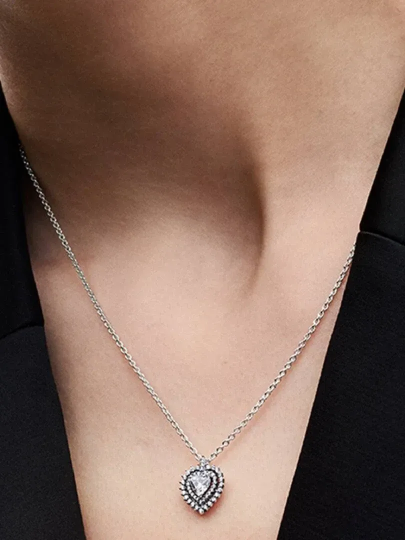 Gros plan du collier avec pendentif cœur porté sur le cou d'un mannequin, fond sombre flou.