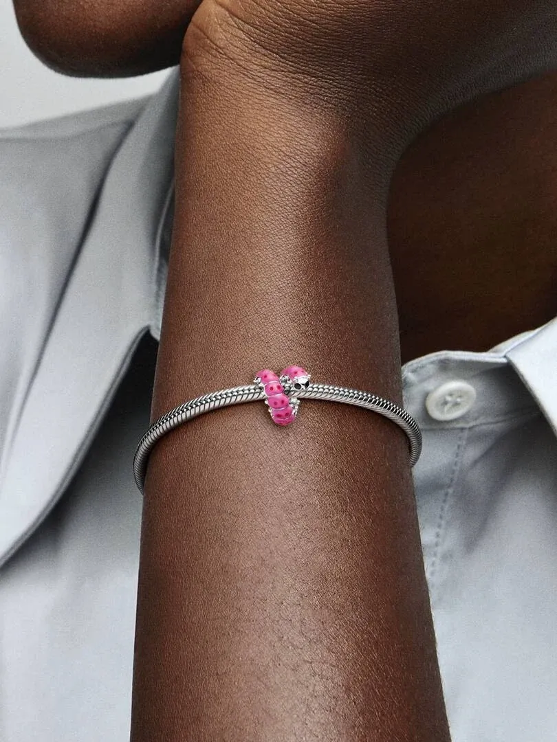 Primer plano de la pulsera con el charm de oruga rosa en la muñeca, toma lateral sobre fondo de camisa blanca.