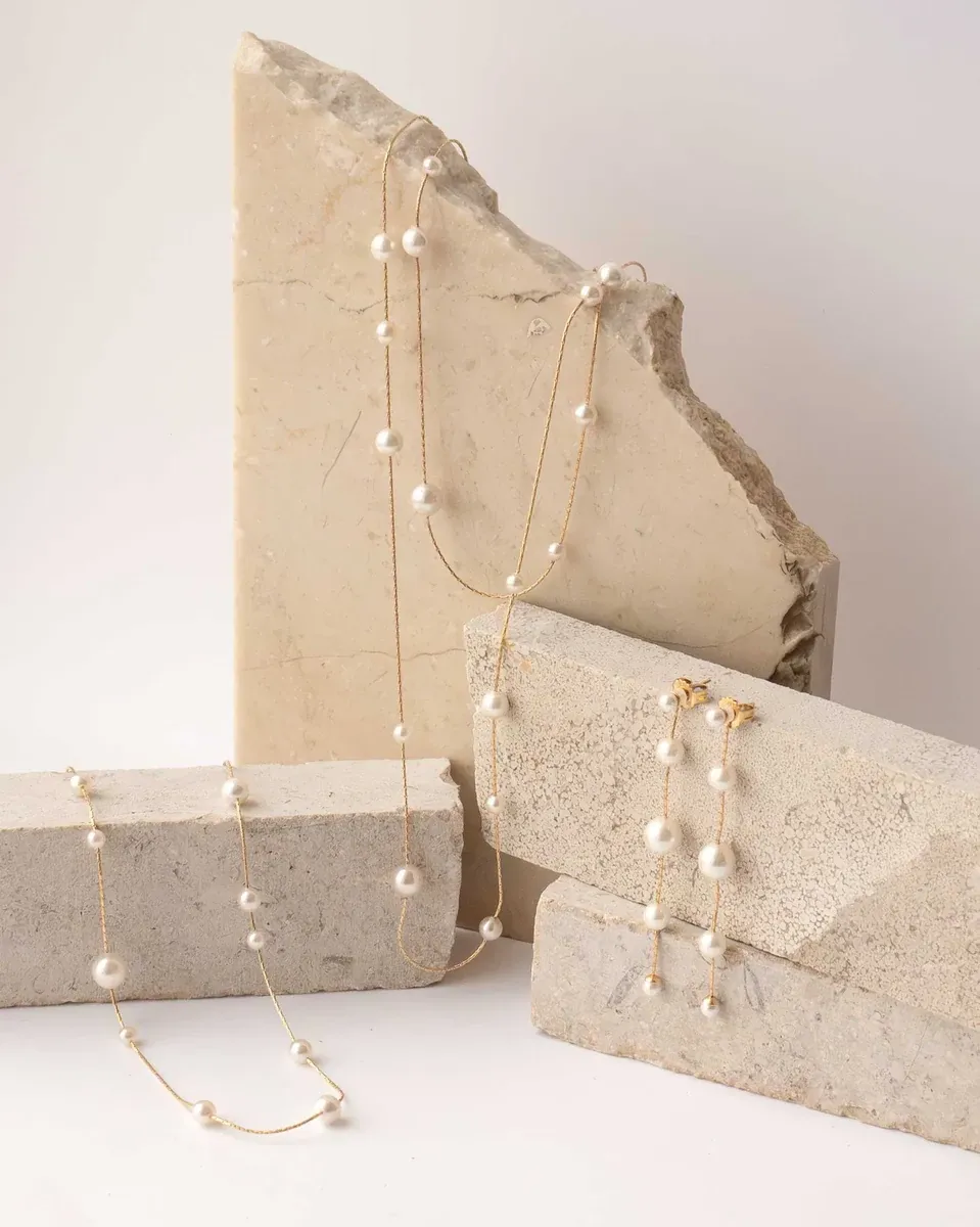 Parelsnoer en oorbellen gerangschikt op natuurstenen blokken, neutrale achtergrond.