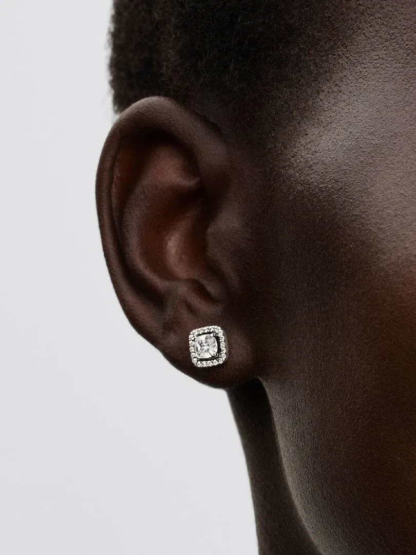 Gros plan latéral d'une boucle d'oreille puces carrée avec halo portée sur le lobe de l'oreille.