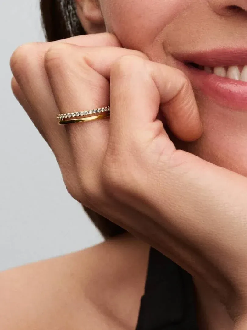 Primer plano de anillo de doble banda con circonitas en el dedo, toma lateral sobre rostro y mano.