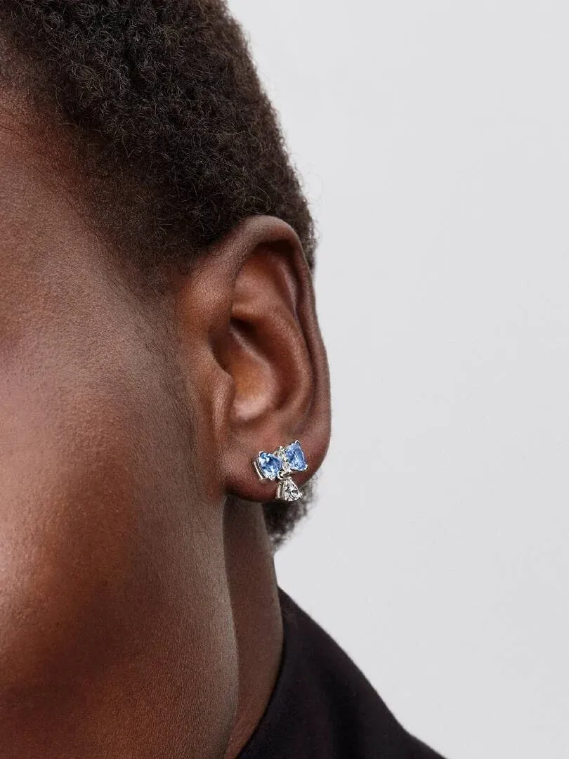 Gros plan latéral d'une boucle d'oreille nœud bleu avec zircon sur le lobe de l'oreille, fond neutre.