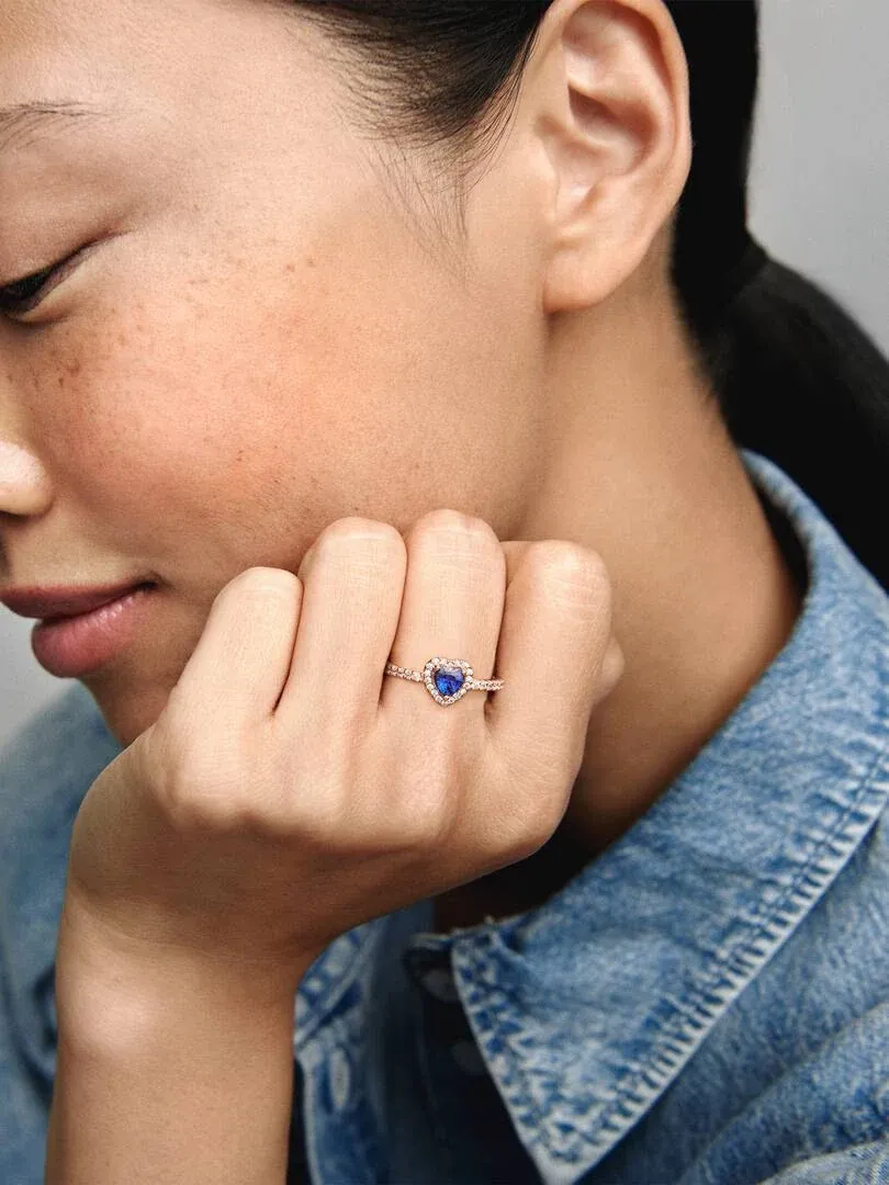 Close-up van blauwe hartring aan ringvinger, model in spijkeroverhemd, zachte zijwaartse opname.