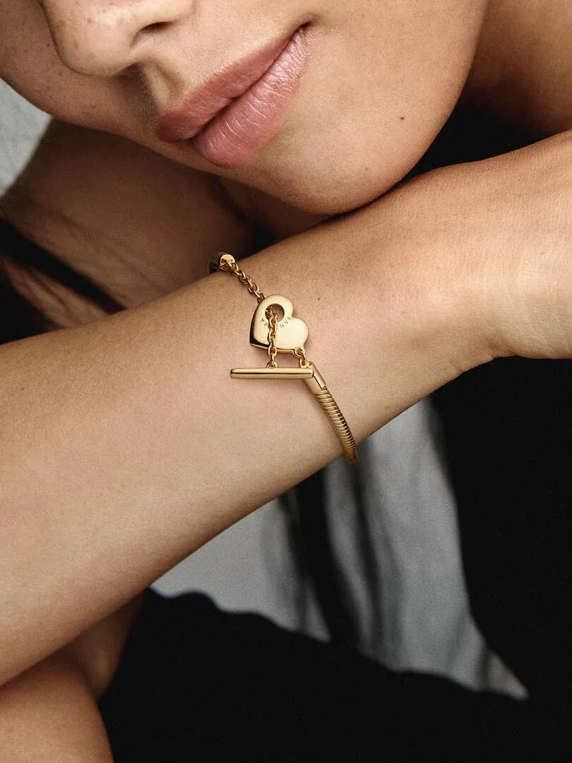 Primer plano de la pulsera con cierre de barra en T y dije de corazón sobre la muñeca, toma lateral.