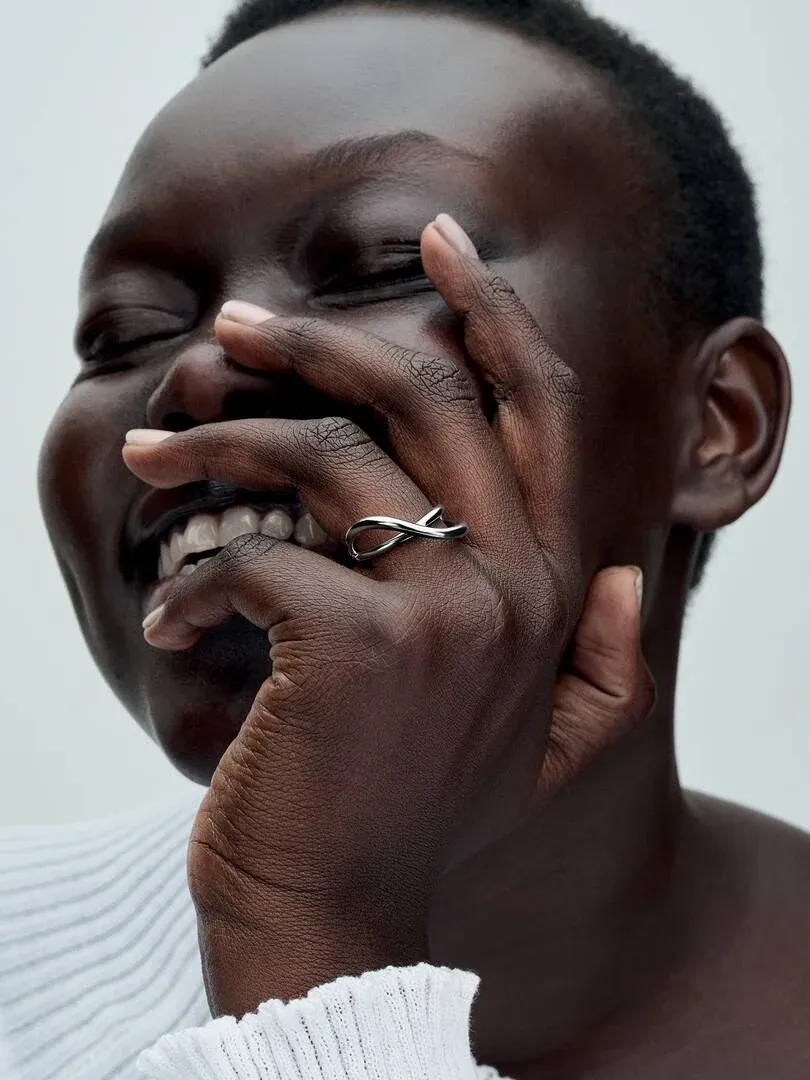 Primer plano de anillo de plata en dedo medio, mano sobre el rostro, fondo neutro claro.