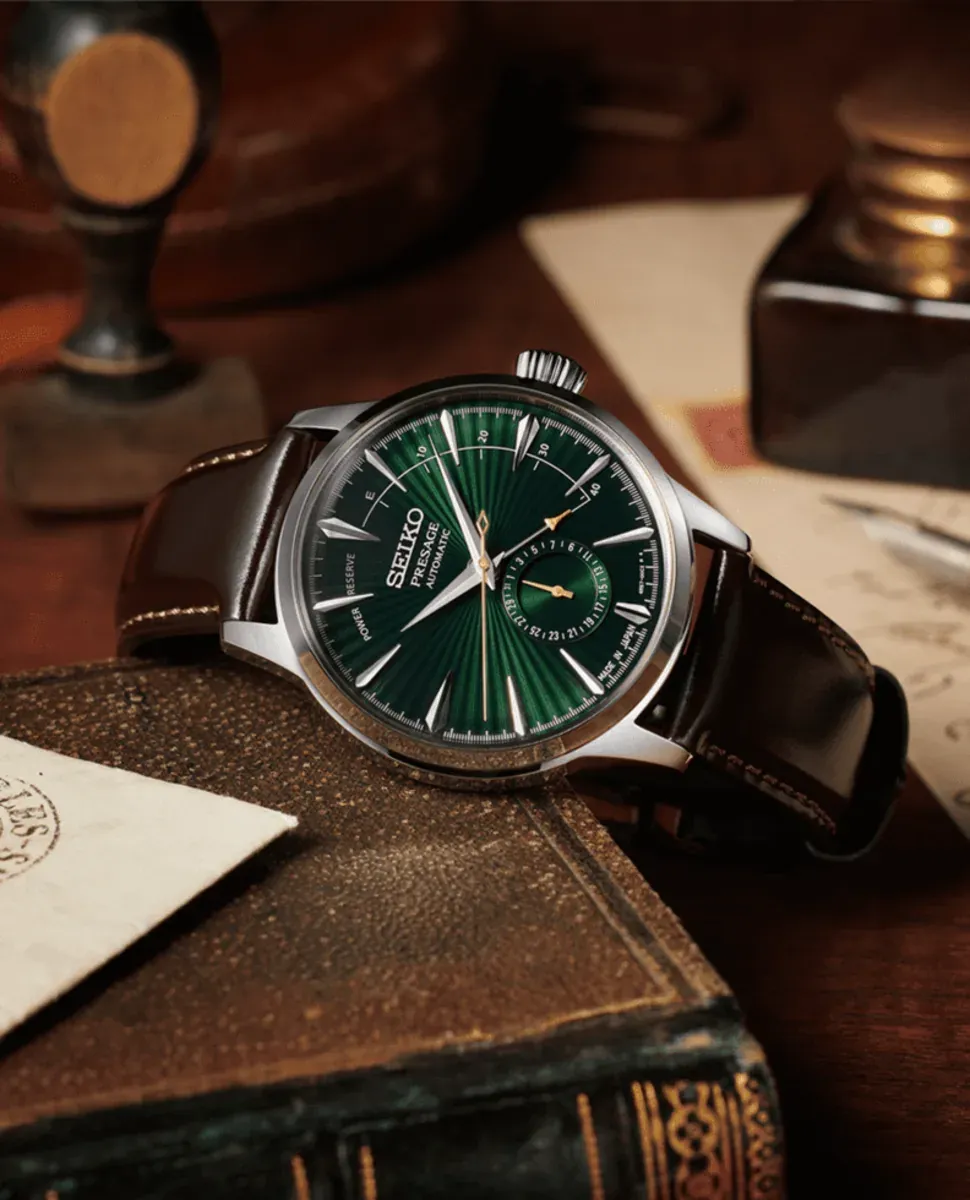 Reloj apoyado sobre un libro antiguo, composición decorativa con fondo oscuro y elementos vintage desenfocados.