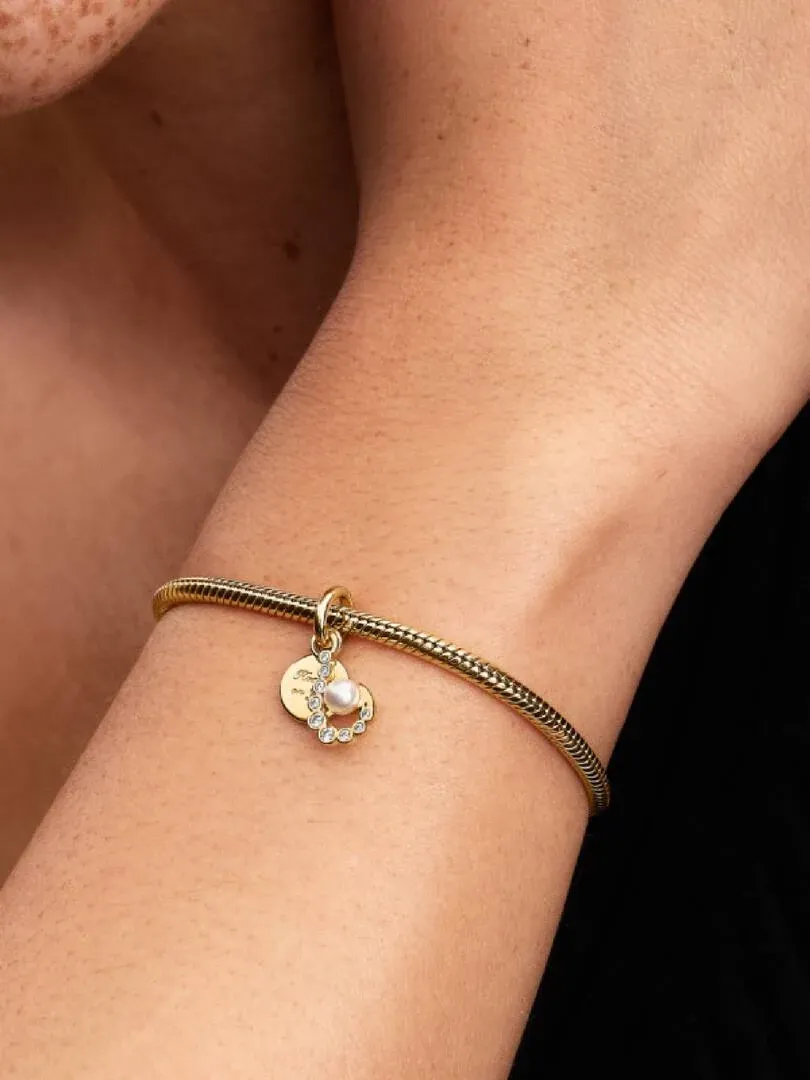 Close-up van de haak en parel charm aan een gouden armband, gedragen om een pols.