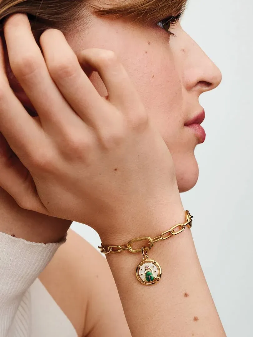 Gros plan latéral d'un poignet avec le charm médaillon scarabée, fond neutre flou.