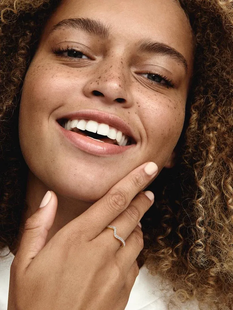 Primer plano de una mujer sonriendo con el anillo ondulado en el dedo, toma lateral enfocada en la mano.