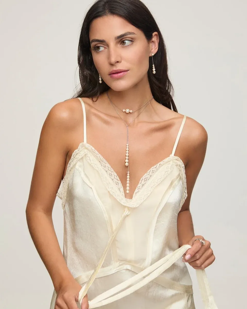 Close-up van model met pareloorbellen en lange ketting, vooraanzicht tegen een neutrale achtergrond.